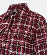 Campera corta de tweed a cuadros en tonos rojo, blanco y negro. Tiene cuello clásico, cierre frontal con botones, dos bolsillos en el pecho y flecos en el dobladillo.