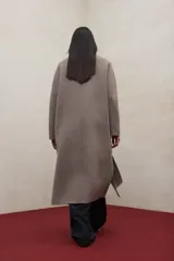 Abrigo largo de lana reciclada en color negro, con diseño minimalista, cuello redondo y cierre frontal con botones ocultos. Presenta aberturas laterales, bolsillos frontales tipo parche y mangas largas.