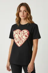 Remera negra de algodón con estampado frontal de un corazón rojo con texto en color crema. Corte holgado y cuello redondo.