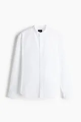 Camisa blanca de corte estándar, con cuello mao, tapeta clásica, canesú en la espalda, mangas largas con puños abotonados y bajo redondeado.