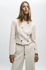 Blazer corta negra de cuello redondo y manga larga, con cierre frontal cruzado con botones dorados y falsos bolsillos delanteros.