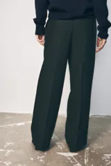 Pantalón negro de tiro alto con pinzas delanteras, pernera ancha y cinturón de cuero con hebilla dorada.