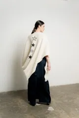 Ruana color crudo de tejido grueso con flecos en el borde inferior y apliques de estrellas bordadas en negro.