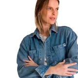 Camisa de jean celeste, de corte amplio, con cuello clásico, cierre frontal con botones, mangas largas con puños abotonados, dos bolsillos con solapa abotonada en el pecho y aberturas laterales en el ruedo.