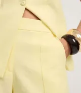 Short de sastrería color amarillo claro, de tiro alto con cintura elástica y cierre tradicional. Presenta frisos verticales en la parte delantera.