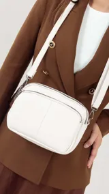 Bandolera pequeña de símil cuero color beige, con dos compartimentos principales con cierre superior y un bolsillo frontal con cierre. Posee correa ajustable para llevar al hombro o cruzada.