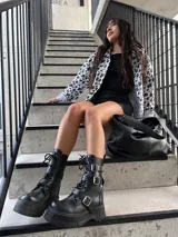 Bota de ecocuero negra con caña media, plataforma y hebillas decorativas.