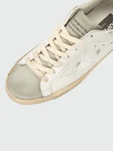Championes Golden Goose modelo Super Star, de cuero blanco con estrella calada en el lateral, talón en cuero negro y suela color crema con efecto desgastado.