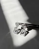 Par de aros colgantes de plata 950, con diseño orgánico y textura martillada. Cada aro consta de dos piezas unidas: una superior redondeada y una inferior cuadrada con un orificio central.