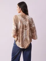 Blusa de crepe color beige con estampado de hojas blancas, cuello redondo con escote en V y lazo de ajuste, mangas 3/4 con tajo.