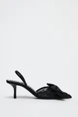 Zapato destalonado negro con tacón fino, capellada de mesh bordado y lazo decorativo en la parte delantera.