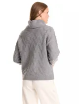 Buzo de punto grueso color beige, con cuello volcado y textura en relieve. Tiene mangas largas de corte hombro caído y puños anchos.