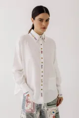Camisa blanca de lino con bordados de colores en cuello, puños y tapeta. Silueta amplia, con bolsillo y doble botón.