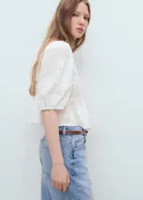 Blusa blanca con bordado floral, cuello de pico, mangas abullonadas tres cuartos y corte peplum.