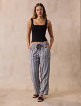 Pantalón largo de lino y rayón a rayas verticales grises y blancas. Tiene pretina elastizada con lazo de ajuste, bolsillos delanteros y traseros.