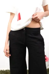 Pantalón blanco de lino, de corte amplio y tiro medio/bajo. Tiene bolsillos delanteros y traseros, botón metálico grabado y bordados laterales y traseros.