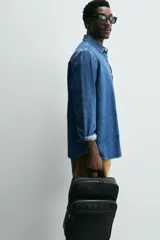 Mochila marrón de cuero sintético con textura grabada. Tiene un compartimento principal con cierre de cremallera, un bolsillo interno para dispositivos electrónicos de hasta 13 pulgadas y un bolsillo interno con cremallera. En la parte delantera tiene un bolsillo con cremallera. La parte posterior es acolchada y tiene una banda de sujeción para equipaje. Tiene un asa de mano y dos asas de hombro ajustables y acolchadas.