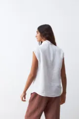 Camisa blanca sin mangas, con cuello clásico y cierre frontal con botones.