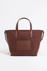 Bolso shopper mediano color marrón chocolate, con doble asa de mano y correa larga extraíble. Presenta un bolsillo rectangular con el logo de la marca en la parte frontal.