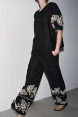 Pantalón culotte negro de lino y viscosa con bordados florales en el ruedo. Tiene tiro medio, cintura con trabillas, bolsillos laterales y cierre frontal con cremallera y botón.