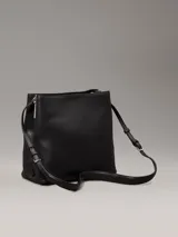 Cartera tipo saco Calvin Klein color negro, con correa ajustable para el hombro, compartimento central con cremallera, compartimento con cierre giratorio en la parte delantera, compartimento magnético en la parte trasera y herrajes plateados con el monograma de la marca.