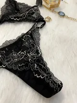 Conjunto de lencería de encaje negro con blanco, compuesto por un corpiño triangular con breteles regulables y cierre de gancho delantero, y una tanga regulable.