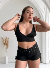 Short negro ajustado con cintura ancha adornada con tachas plateadas y lazos laterales.