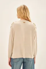 Sweater color beige con cuello redondo y mangas largas. Presenta apliques dorados en los hombros y un cinturón marrón con forma de flor.