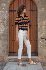 Chomba tejida de punto con cuello estilo polo y escote en V. De manga corta y calce relajado, cuenta con diseño de ondas horizontales en colores combinados: negro, naranja, blanco y lila.