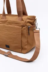 Cartera de nylon color verde militar con asas superiores reforzadas y correa larga regulable y desmontable. Cuenta con bolsillos frontales y laterales con cierre metálico, y un logo de la marca en la parte inferior central.