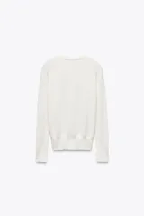 Sweater negro de punto liso con cuello redondo y mangas largas con botones dorados en los puños.