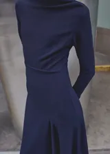 Vestido midi azul marino de corte evasé, con cuello barco, manga larga, cintura fruncida, bajo asimétrico y cierre de cremallera en la parte posterior.