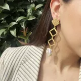 Caravanas de metal dorado mate con perlas barrocas, con diseño de rombos y movimiento.