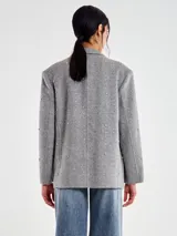 Blazer de mezcla de lana color gris oscuro, con apliques tipo joya en forma de puntos dispuestos en líneas verticales. Presenta solapas de muesca, cierre frontal de un solo botón y bolsillos de parche delanteros.