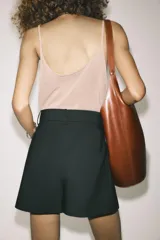 Shorts de tiro alto color negro, con cintura con trabillas, bolsillos laterales y cierre frontal con cremallera y ganchos metálicos.