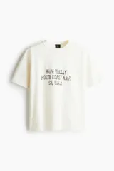 Remera de corte holgado en punto de algodón color crema, con cuello redondo acanalado y estampado con texto en el frente.