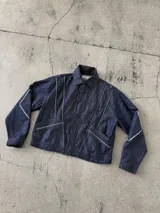 Campera de jean negra tipo bomber con cuello redondo y cierre frontal con botones metálicos. Presenta un parche rectangular con diseño gráfico en la espalda.