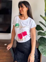Remera blanca de algodón con cuello redondo y estampado de cerezas rojas con hojas verdes y texto dorado.