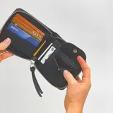 Billetera negra de cuero sintético con cierre alrededor y logo de la marca en el frente.