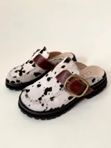 Zueco tipo mule negro, confeccionado en cuero vacuno, con puntera cuadrada y suela track gruesa. Presenta una faja ancha con hebilla metálica plateada sobre el empeine.