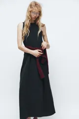 Vestido midi negro de cuello redondo y sin mangas. Corte amplio y fluido, con bolsillos laterales ocultos y cierre trasero con cremallera invisible.