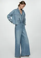Mono largo de jean celeste con corte wide leg, sin mangas, escote en V, bolsillos de parche en el pecho y laterales, trabillas y cierre frontal con botones.
