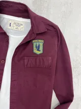 Sobrecamisa de gabardina color burdeos, con dos bolsillos en el frente y parches decorativos.