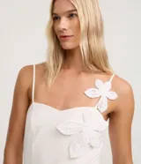 Mono blanco de piquet con tirantes finos, escote corazón y apliques de flores de tejido en relieve sobre el busto y el hombro. El pantalón es de corte ancho y recto.