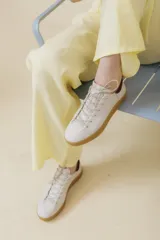 Zapatillas bajas de cuero color blanco hueso, con cordones finos y suela color caramelo.