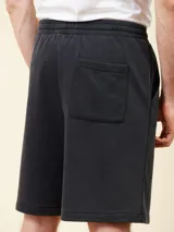 Bermuda de felpa negra con cintura elástica ajustable con cordón blanco. Presenta un estampado con un sol y el logo de la marca en la pierna derecha.