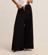 Pantalón negro de sastrería, corte palazzo, con elástico en la cintura trasera y cinturón con hebilla metálica.