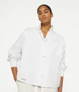 Camisa blanca de corte holgado confeccionada en piqué de algodón orgánico. Presenta un bolsillo de parche en el pecho, puños de forro polar con borde sin rematar, cuello sin rematar con cierre de botón, bajo redondo, minirayas bordadas en la espalda y un estampado Unexpectedly Simple Amsterdam en la costura del lado derecho.