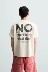 Camiseta color crema de corte cuadrado, con cuello redondo y mangas cortas. Estampado frontal con la frase "no matter what day" en letras pequeñas de color negro.
