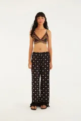 Pantalón negro con estampado de flores y piñas, corte holgado, tiro medio con elástico en la cintura y ruedo con volados.